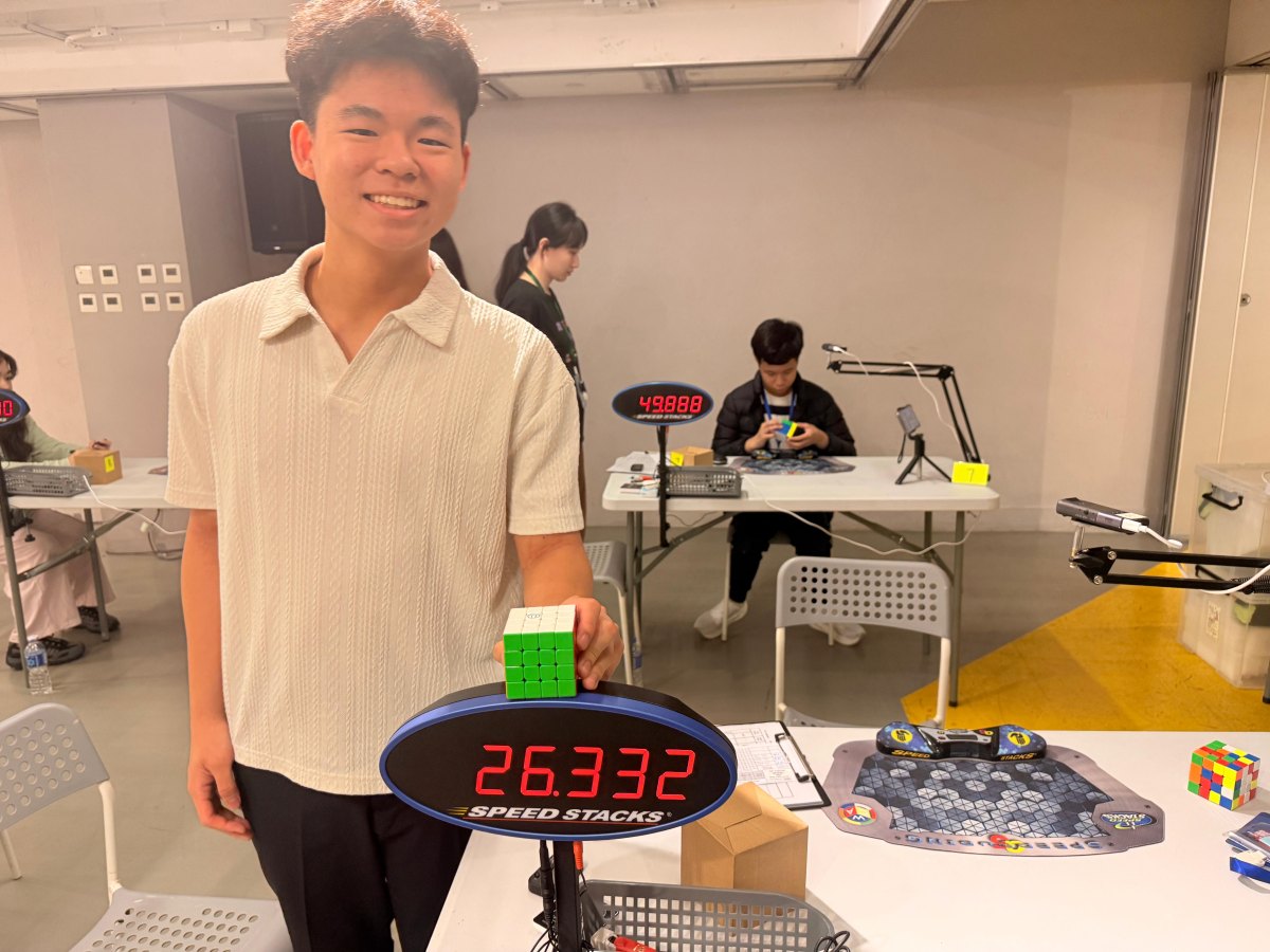 Jeco holding a 4×4 cube beside a competition timer showing 26.332 seconds